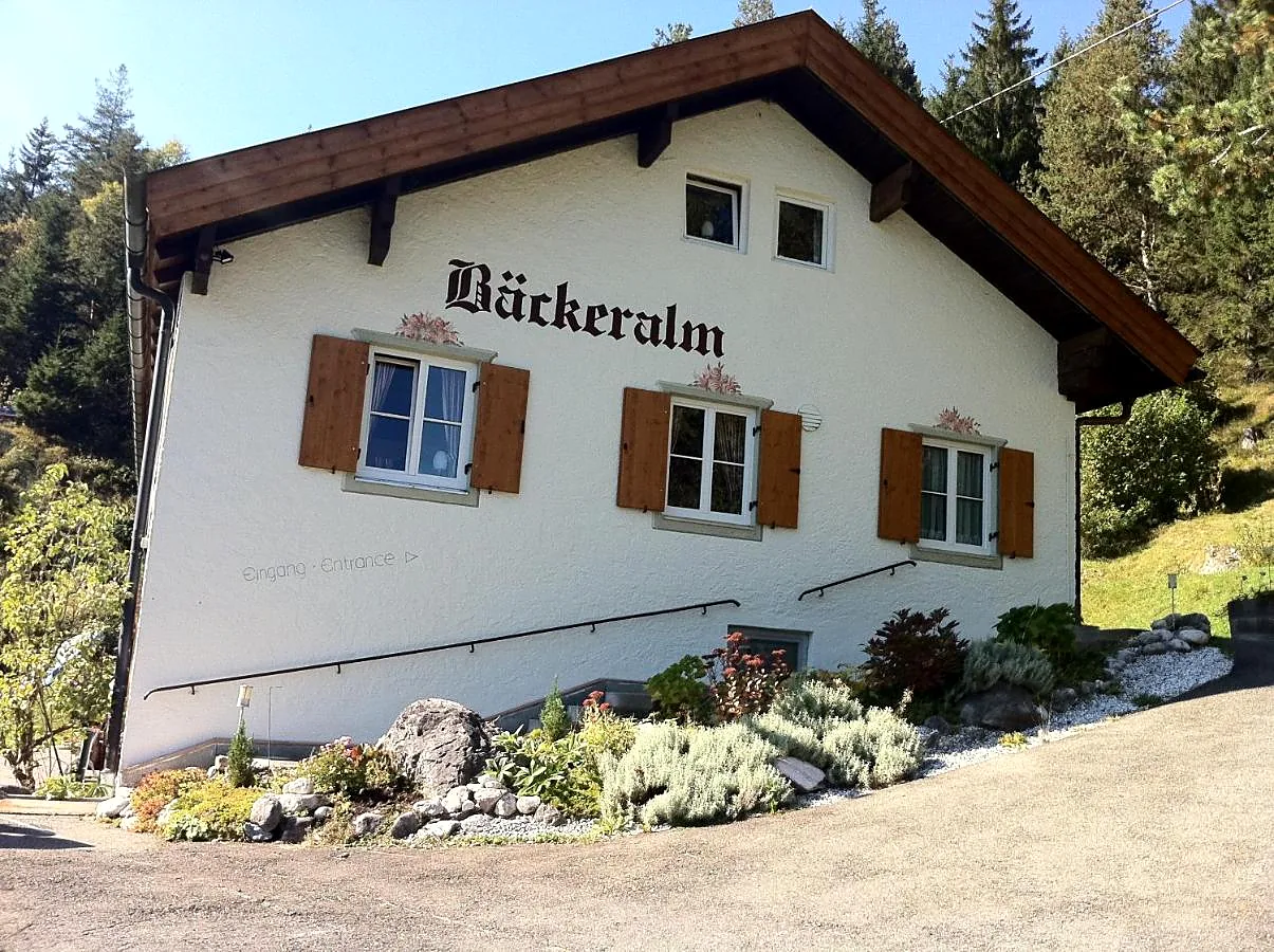 Die Bäckeralm: weiß verputztes Haus mit braunen Fensterläden und dem gemalten Schriftzug Bäckeralm an der Giebelseite