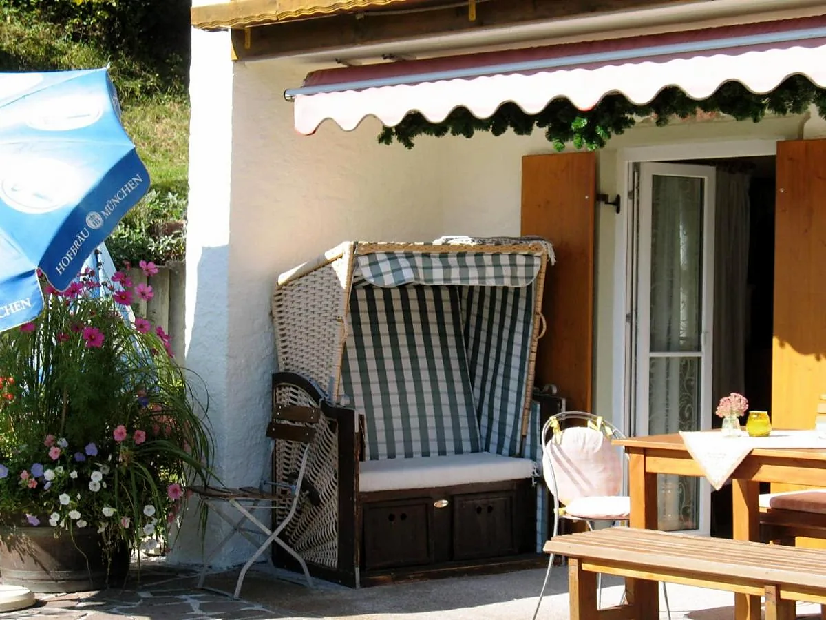 Terrasse vor dem Haus mit Strandkorb, Holzbank, Tisch und Blumen unter der Markise
