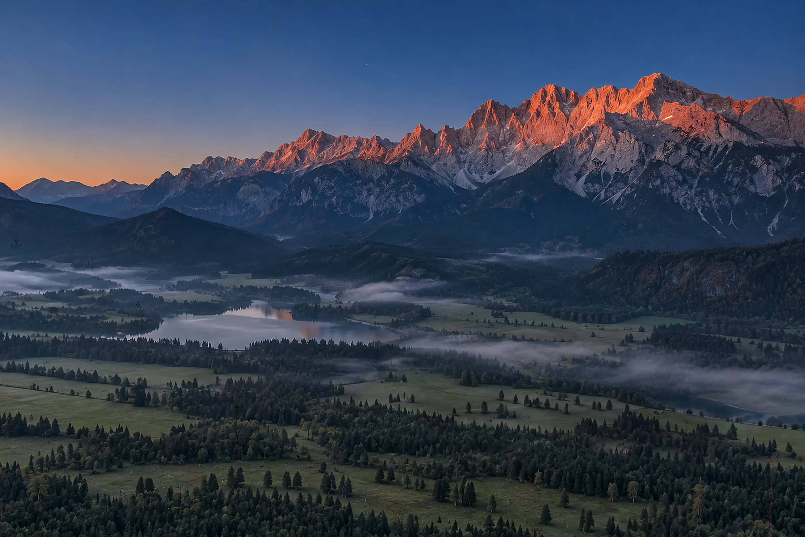 Abendrot an den Gipfeln des Karwendels, unten liegt das Tal mit einem See schon im blauen Dunst (Illustration)